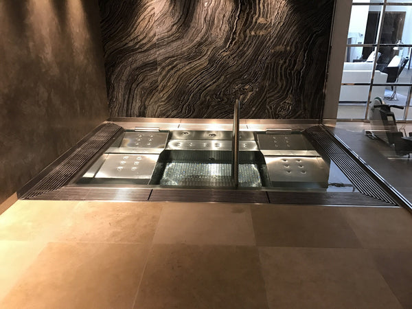 Spa en inox sur mesure encastré dans un sol en pierre, avec banquettes, buses et main courante