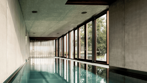 Piscine miroir intérieure en inox à Mourcourt, bordée de grandes baies vitrées ouvertes sur le jardin