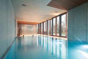 Piscine intérieure en inox à débordement, murs en béton et baies vitrées, à Mourcourt en Belgique