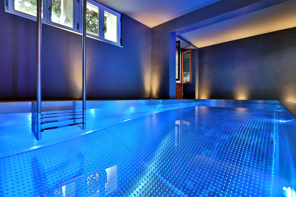 Piscine intérieure en inox éclairée en bleu, échelle inox et soupiraux, dans une villa à Hossegor